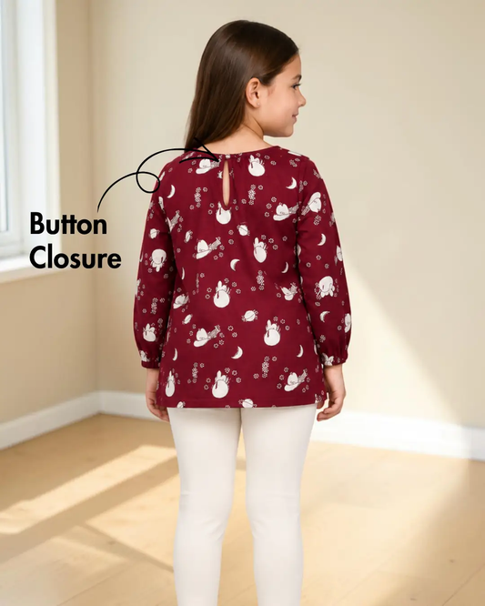 Back view of a girl in a red long sleeve blouse with a snowman pattern, elastic sleeve hems, and white pants, standing in a room.