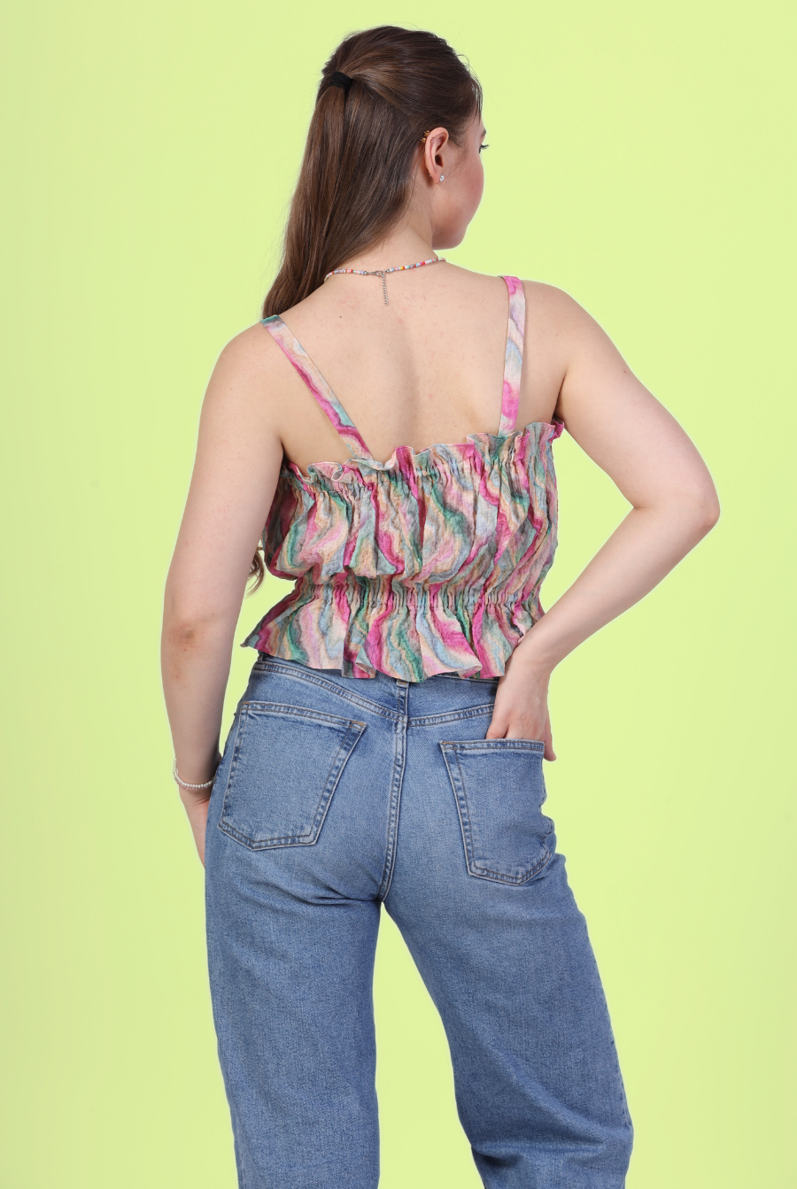 Back pose of woman wearing a strappy ruffle top with blue jeans