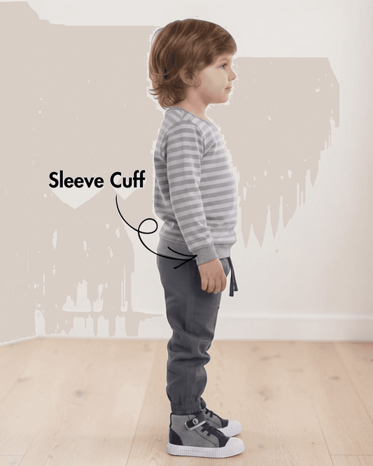 Side view of child in gray sweatshirt with optional bottom band, wearing dark gray pants, standing indoors