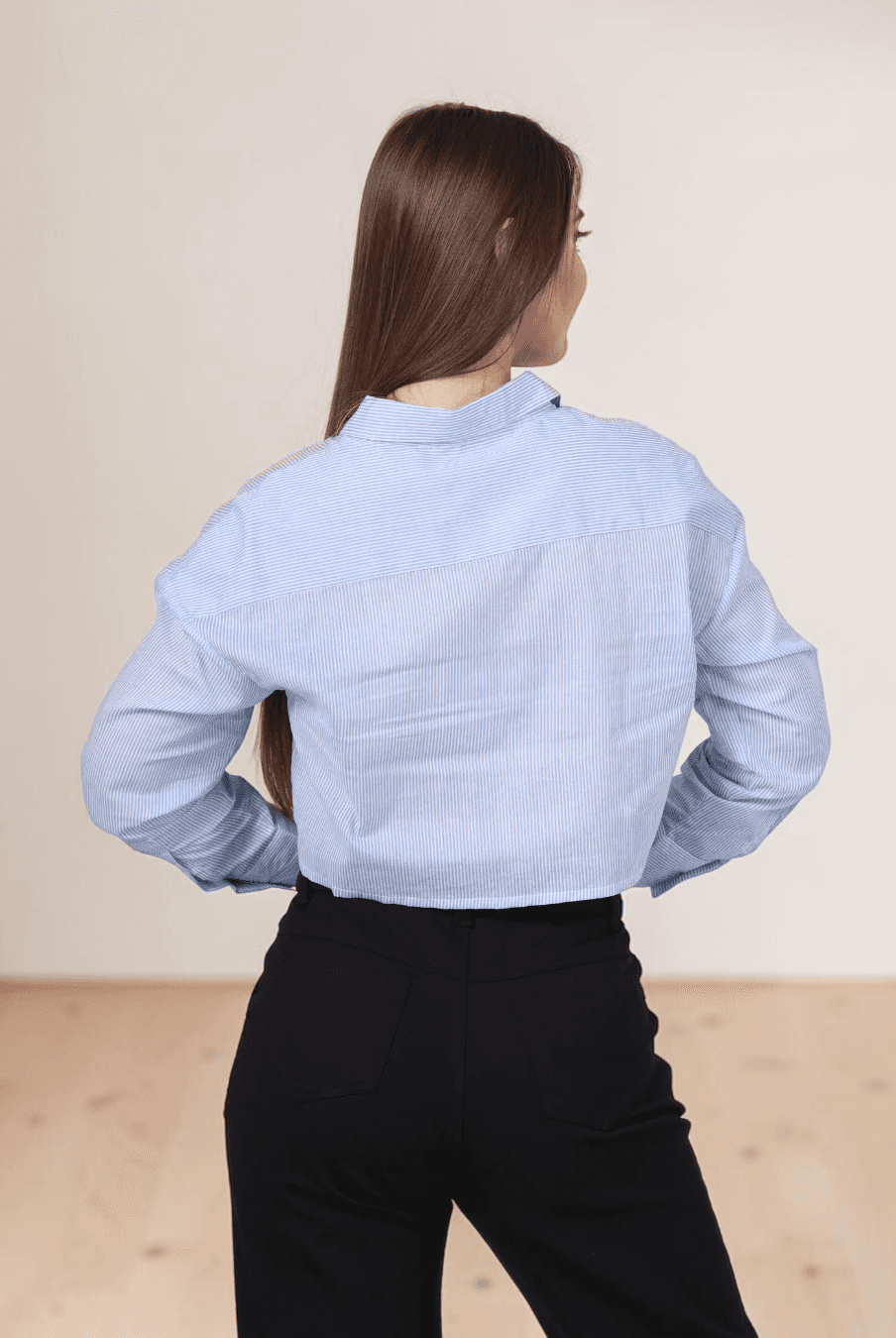 Back view of woman in blue striped utility shirt with point collar and long sleeves, paired with black pants