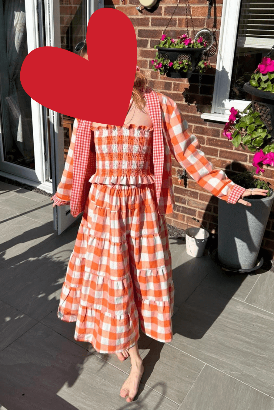 Model wearing the Reversible Quilted Jacket 'Romy' in orange gingham, styled open over a matching dress, showcasing long sleeves and contrast binding.