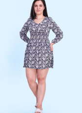 Model wearing the Donna Shirred Dress with a floral print. This mini dress features a smocked bodice, long sleeves, and a flared skirt for all occasions.