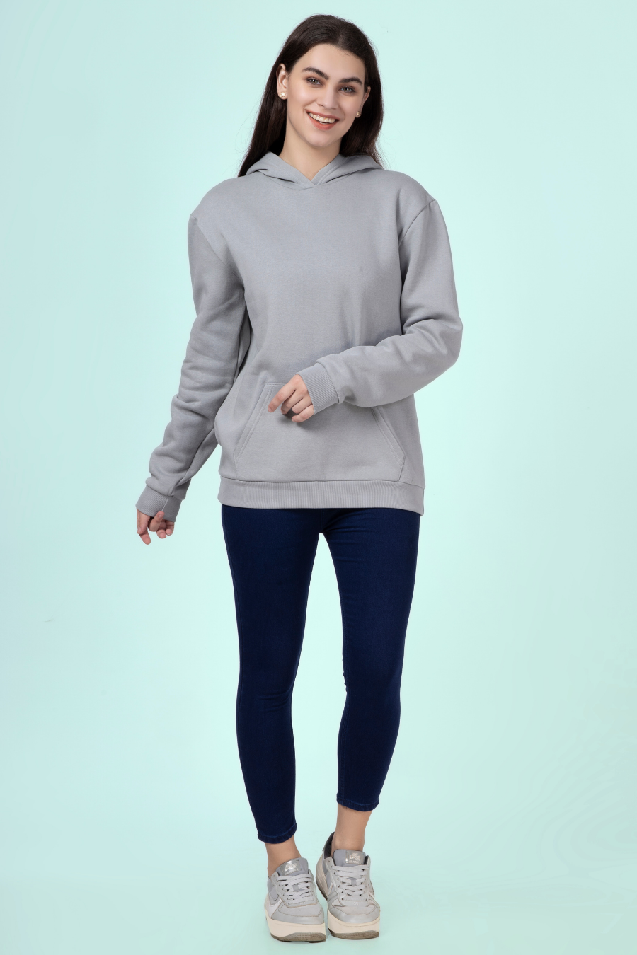 Full-body view of a woman wearing a gray hoodie and dark leggings, demonstrating the casual and versatile style of the 'Rhea' sewing pattern.