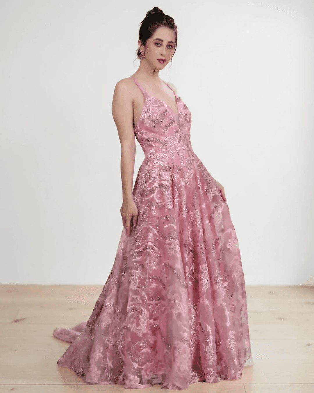 Model wearing pink floral lace evening gown with plunging neckline, flowing gathered skirt, delicate straps, low scoop back, side view