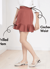 Model wearing rust-colored flounced hem mini skirt with cinched waist and back zipper