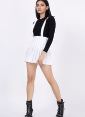 Model wearing a suspender skirt with adjustable straps and high-waist pleats, paired with a black top