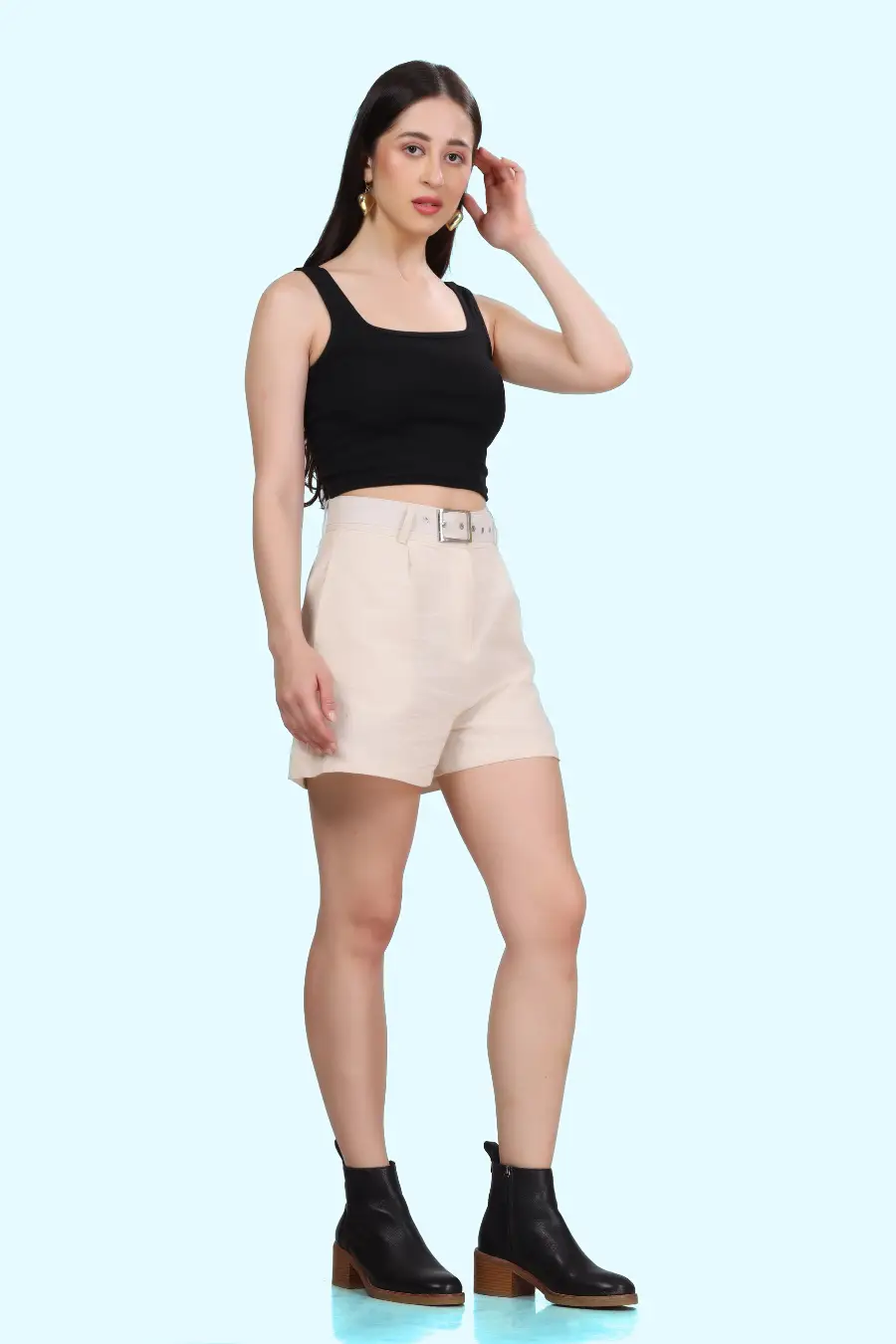 Side view of model wearing high-waisted shorts with coordinating belt and pleat details, paired with a black top.