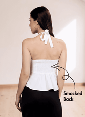 Back view of white halter top with smocked back panel, model in black skirt