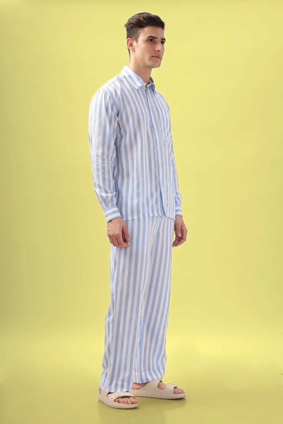 Side view of a model in a blue and white striped men's pajama set from the 'Arbor' sewing pattern. Comfortable fit with a classic button-up design.