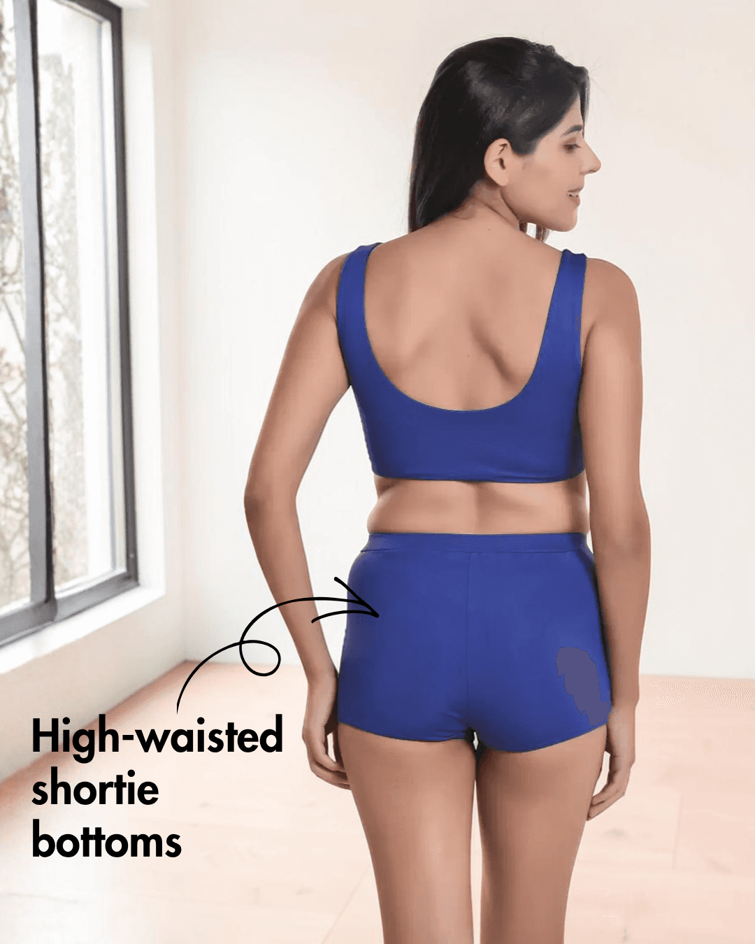 Back view of woman in blue sports bikini with deep scoop neckline and high-waisted shorts