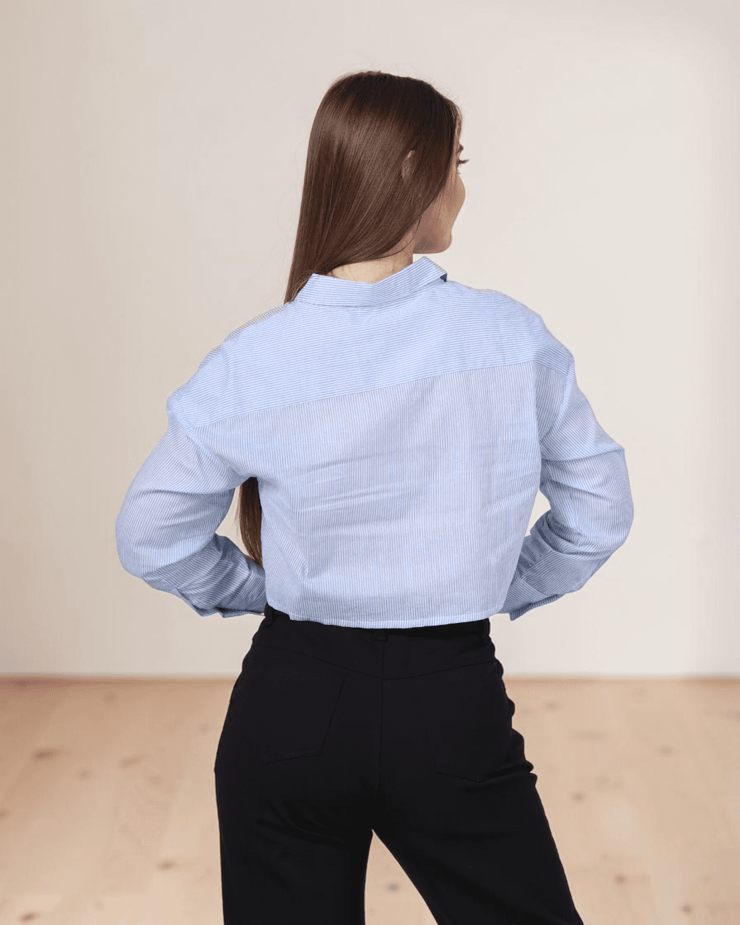 Back view of woman in blue striped utility shirt with point collar and long sleeves, paired with black pants