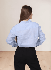 Back view of woman in blue striped utility shirt with point collar and long sleeves, paired with black pants