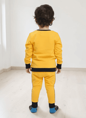 Back view of a young boy wearing yellow kids' leggings with black cuffs, paired with a matching yellow sweatshirt, standing in a bright room