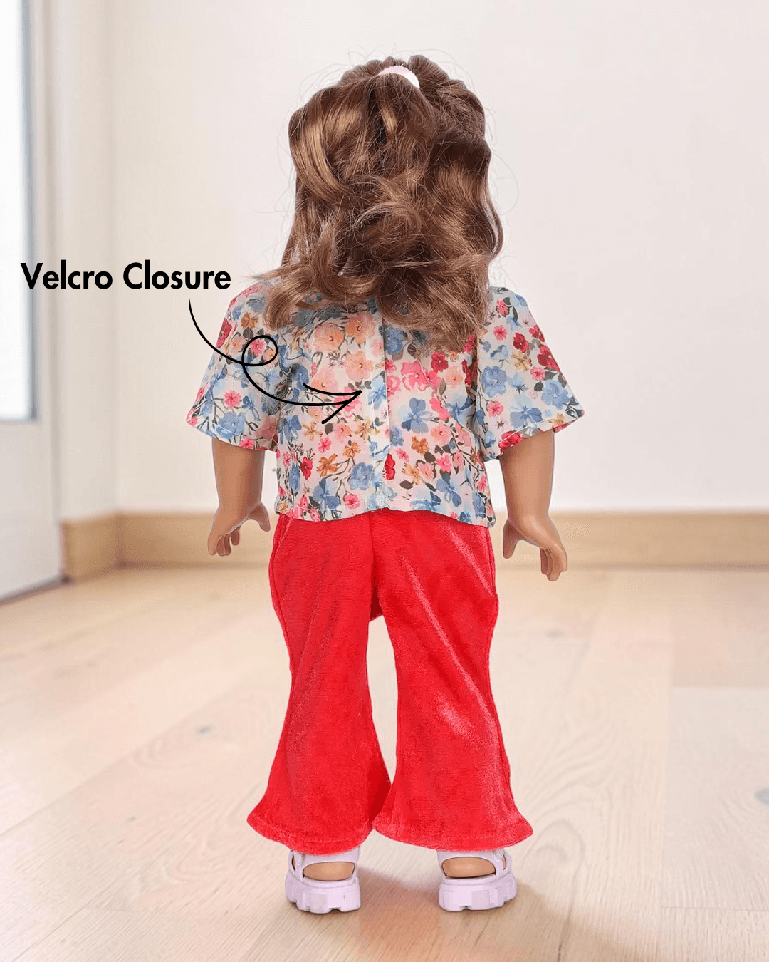 Back view of doll with floral top, red pants, and pink sandals, showing velcro closure