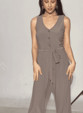 Model wearing taupe sleeveless jumpsuit with button front and waist tie