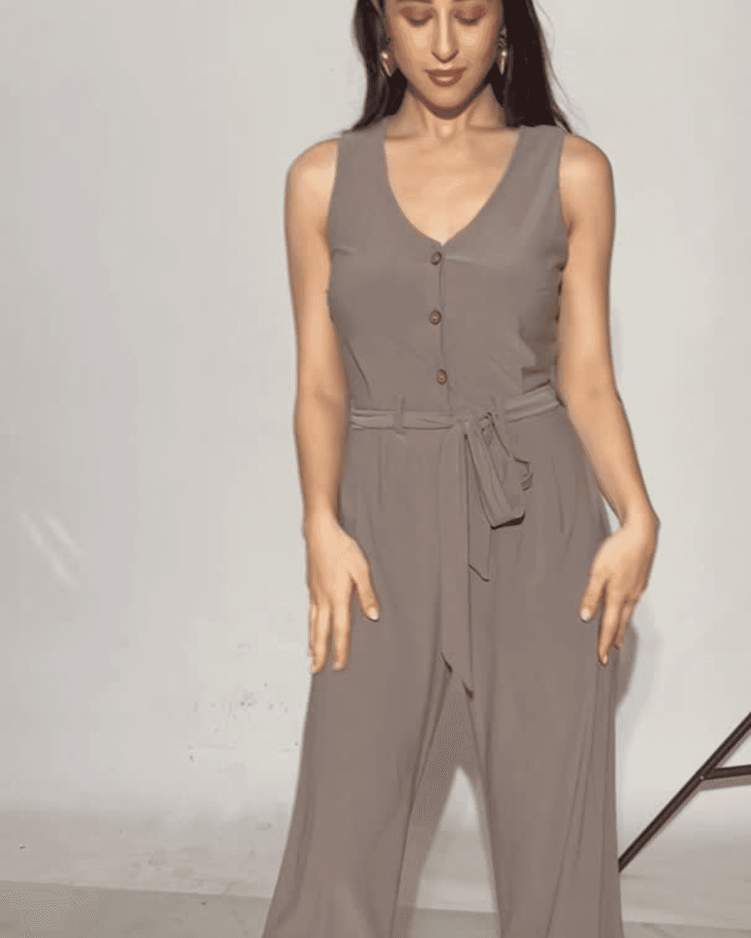 Model wearing taupe sleeveless jumpsuit with button front and waist tie