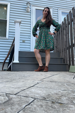 Model wearing a green floral Donna Shirred Dress outdoors. Features a smocked bodice, long sleeves, and a flared skirt, perfect for casual or dressy occasions.