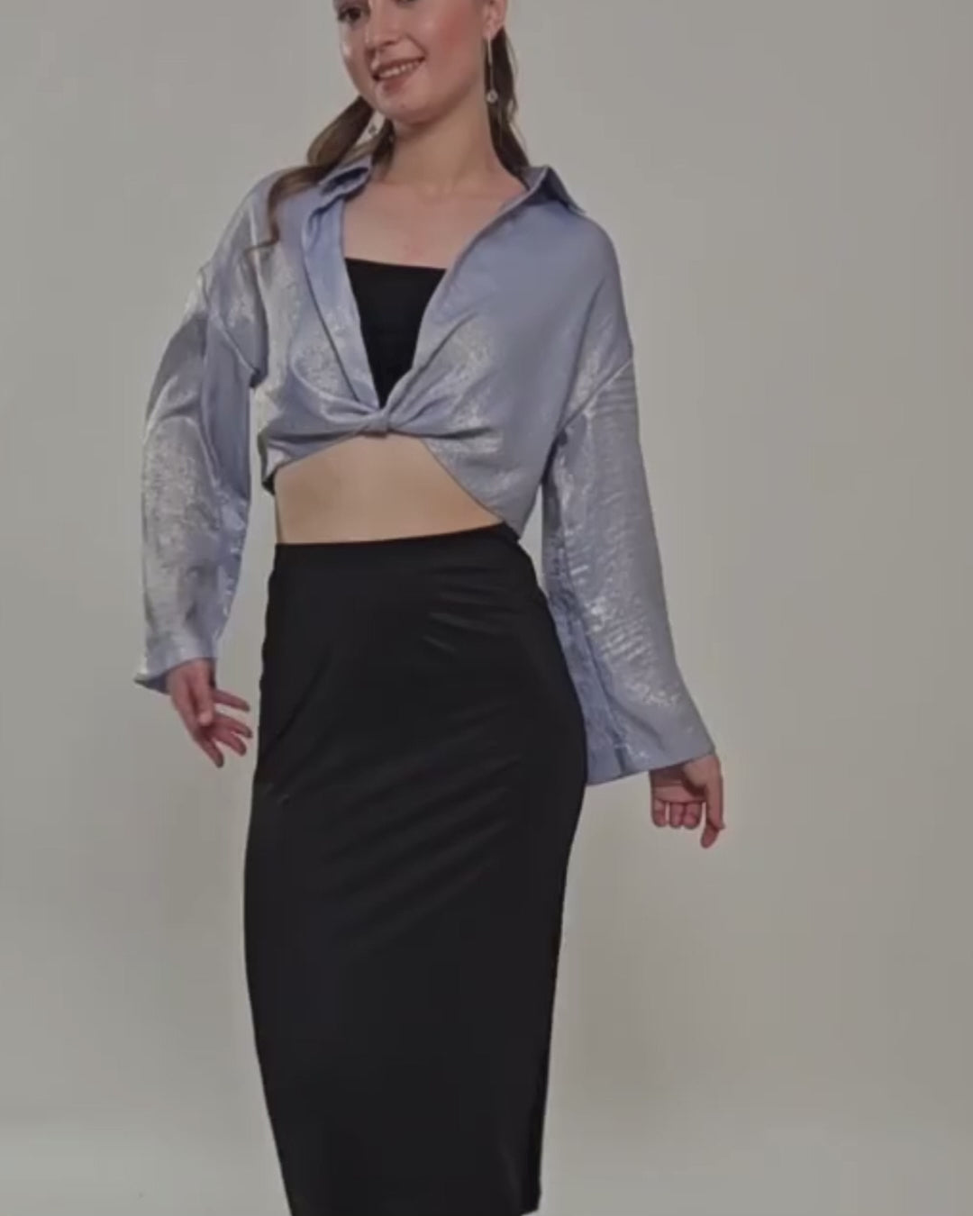 Model wearing a silver twisted front crop shirt with long sleeves and high-waisted black skirt