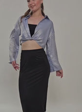 Model wearing a silver twisted front crop shirt with long sleeves and high-waisted black skirt