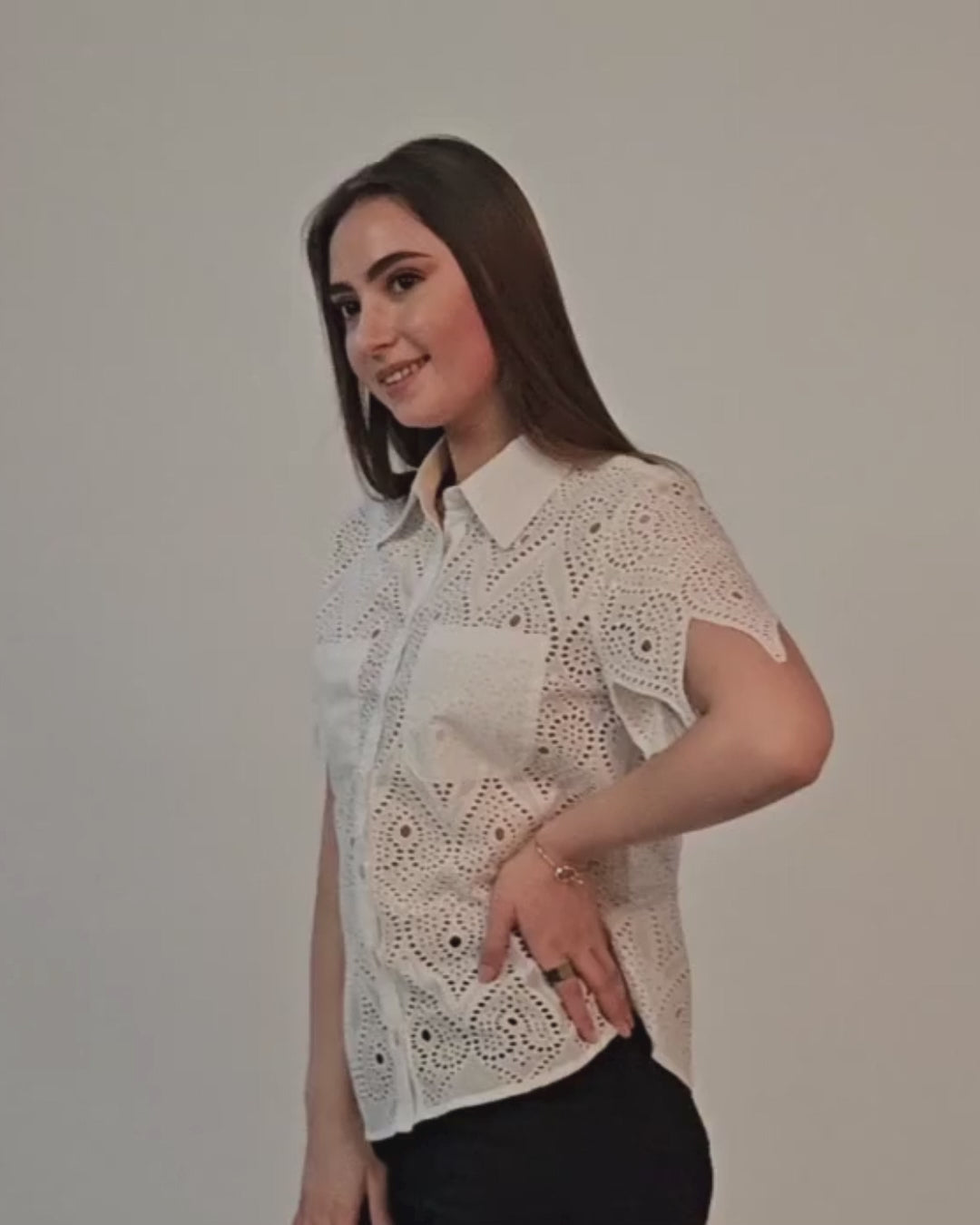 Woman wearing a white lace short sleeve shirt with button front, standing sideways, smiling