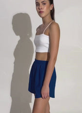 Side profile of a model wearing blue training shorts from the 'Maria' sewing pattern. Showcases the relaxed fit and comfortable waistband.