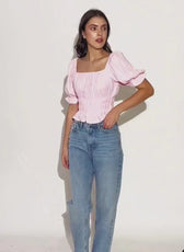 Model wearing pink puff-sleeve blouse with high-waisted jeans, showcasing the Milkmaid Top 'Samara'