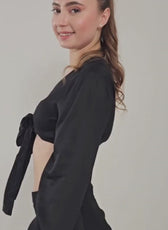 Woman wearing black satin wrap blouse with tied sleeves, side view, elegant fashion style