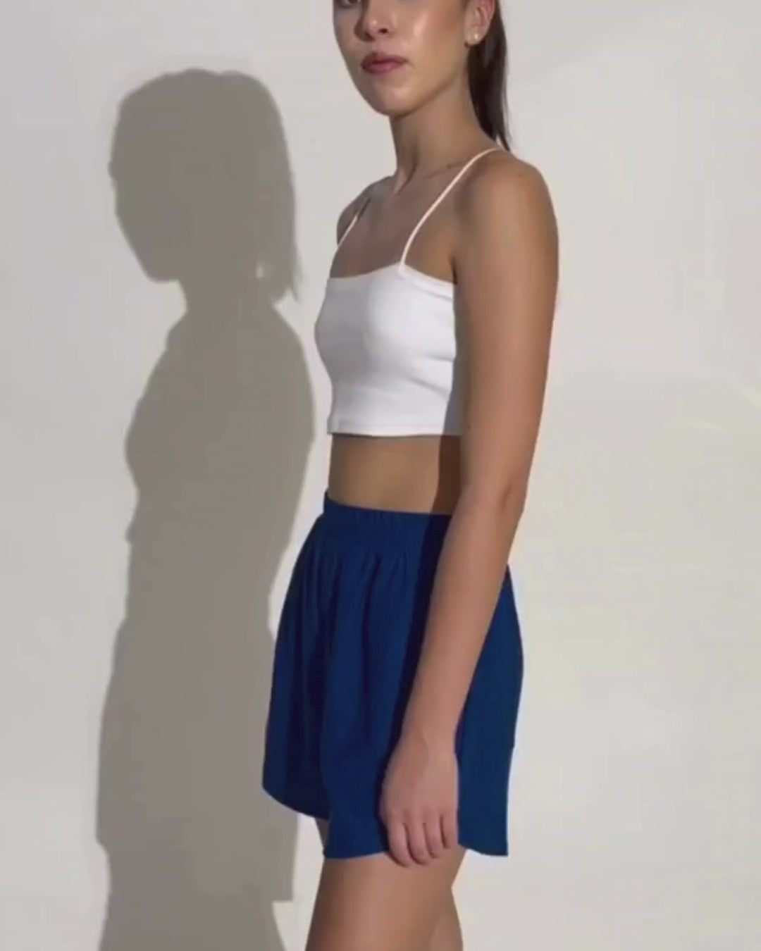 Model wearing white crop top and blue shorts, demonstrating athletic shorts style
