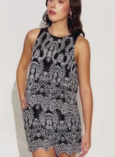 Model wearing black and white embroidered sleeveless dress with wide straps, floral pattern, and scalloped hem