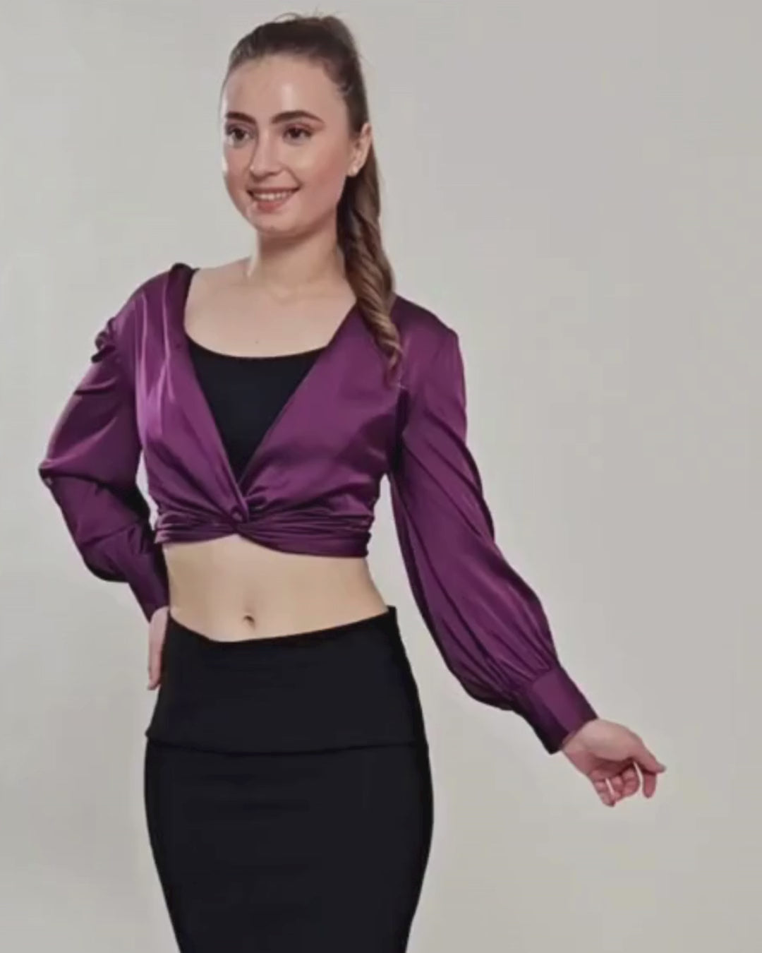 Woman modeling purple satin crop top with long sleeves and twist front design