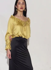 Woman wearing yellow satin peasant blouse with ruffled neckline and long sleeves