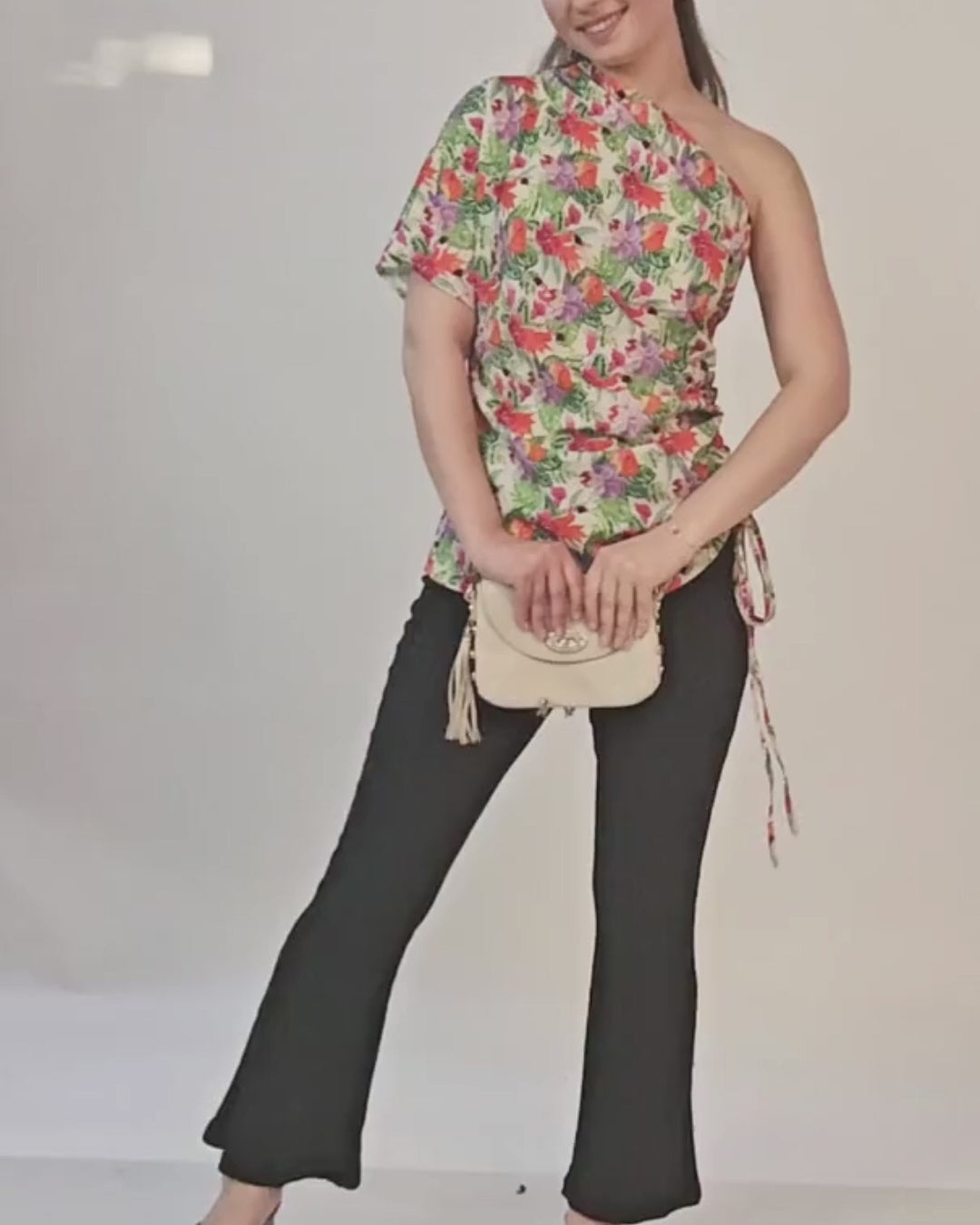 Photo of woman wearing floral one shoulder kimono top with side tie, paired with black pants and small handbag